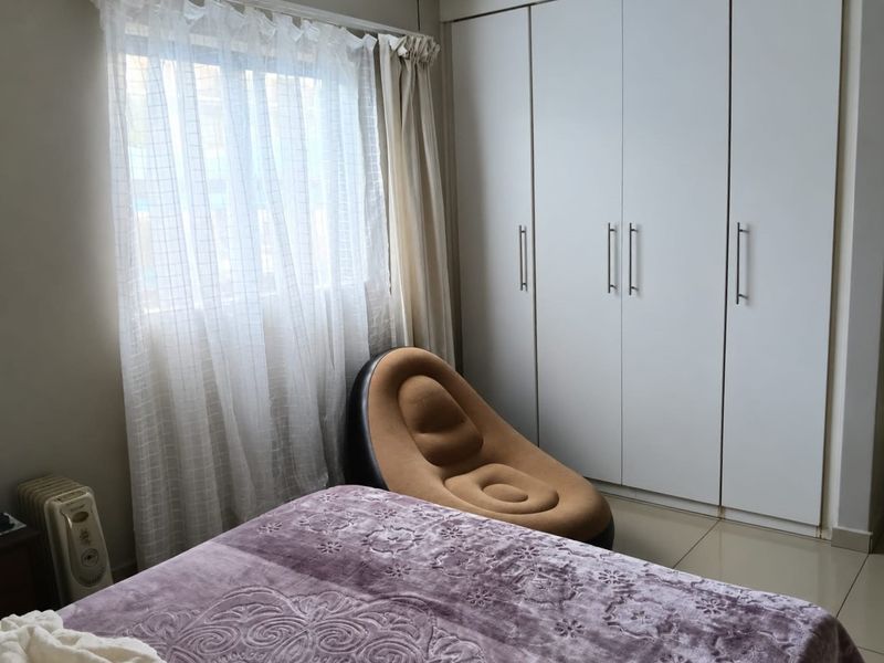 A bedroom featuring built-in white cupboards and tiled flooring, offering a functional space with natural light from the window.
