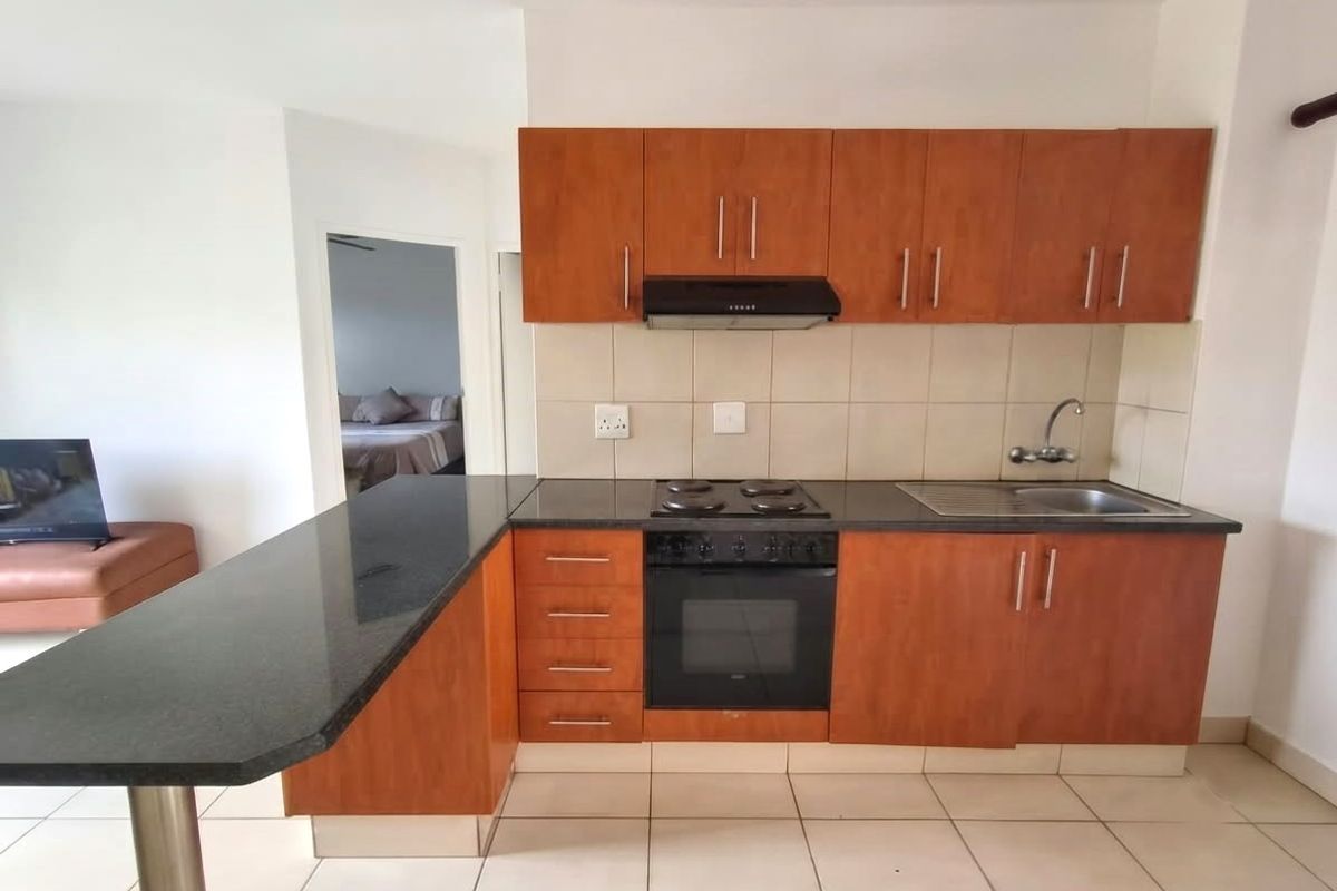 Functional kitchen featuring wood-finish cabinetry, granite countertops, integrated oven and hob, and a breakfast bar, with tiled flooring throughout.