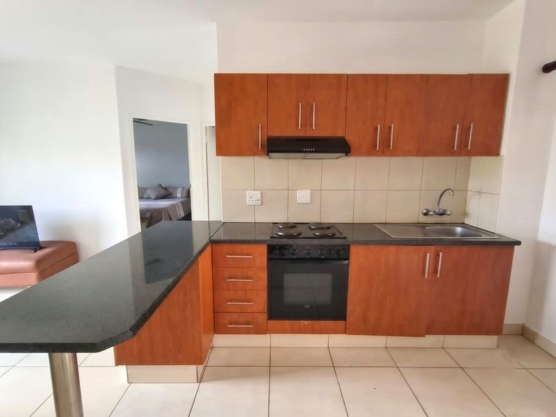 Functional kitchen featuring wood-finish cabinetry, granite countertops, integrated oven and hob, and a breakfast bar, with tiled flooring throughout.
