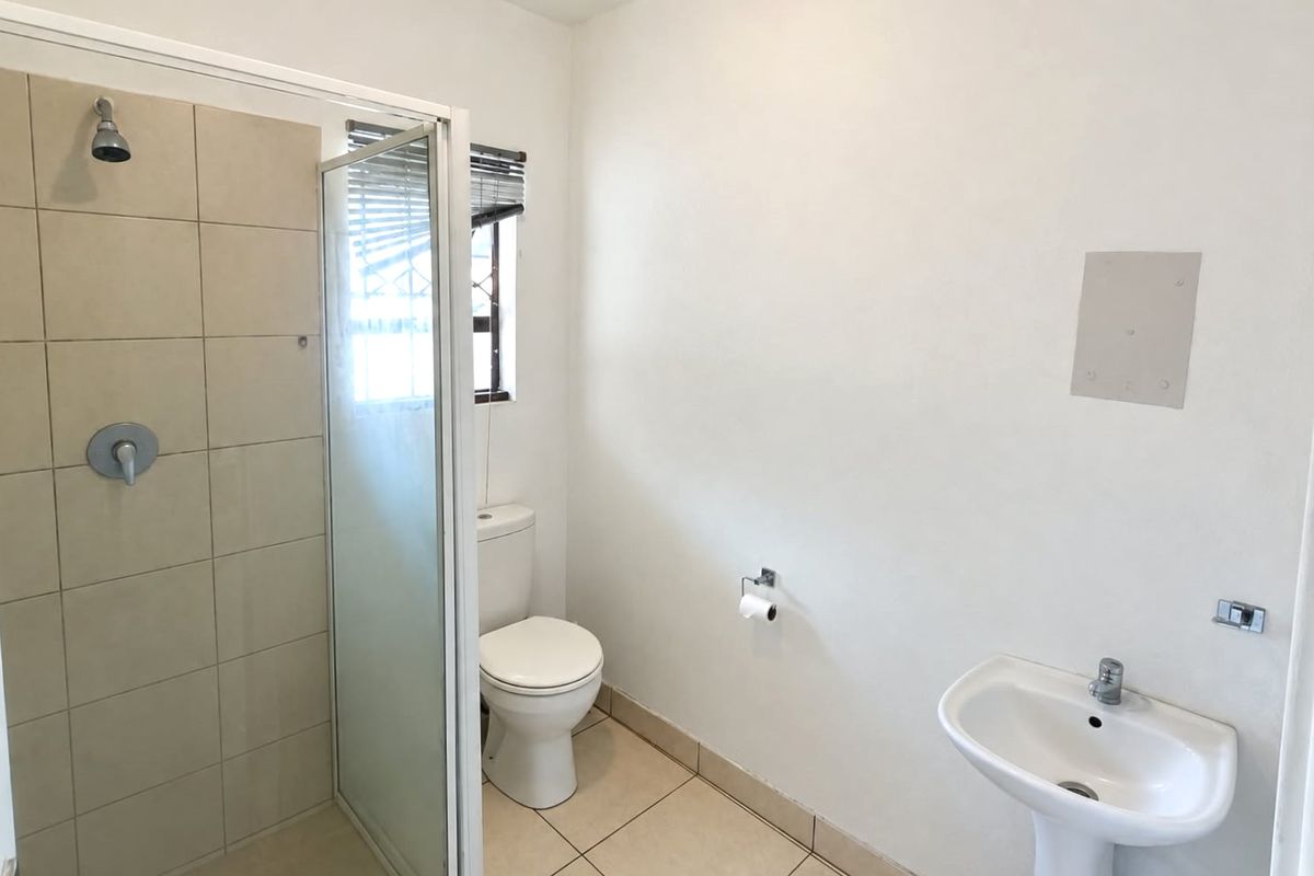 A functional bathroom featuring a tiled shower enclosure, pedestal basin, and toilet, with neutral finishes and natural light from a window.