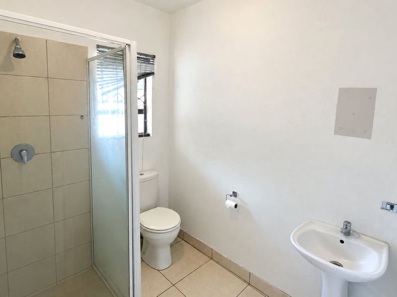 A functional bathroom featuring a tiled shower enclosure, pedestal basin, and toilet, with neutral finishes and natural light from a window.