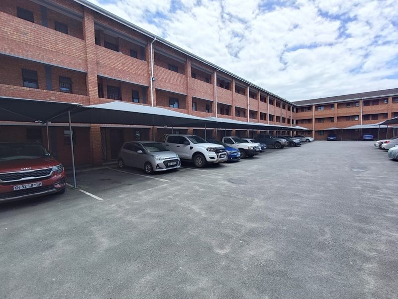 Exterior view of a multi-story brick apartment complex featuring covered parking bays and paved driveway access.