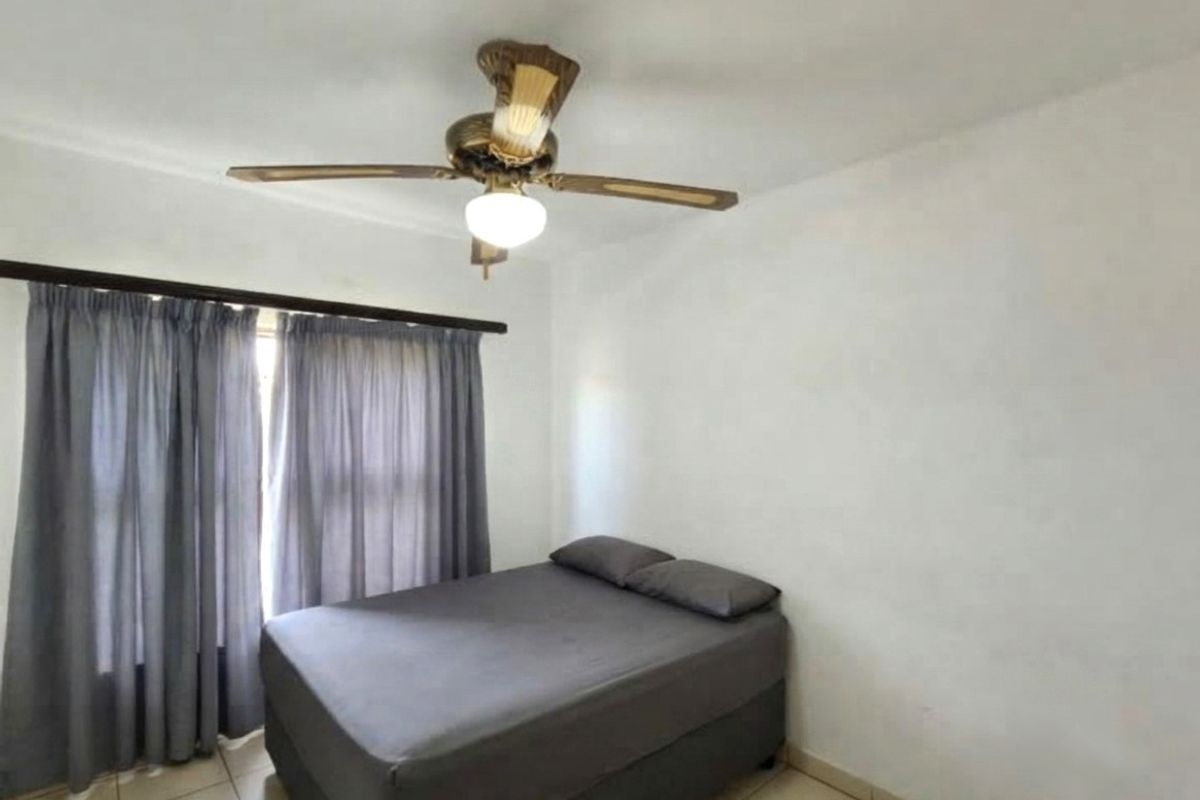 A simple bedroom featuring tiled flooring and a ceiling fan, providing a functional space with neutral walls and window treatments.