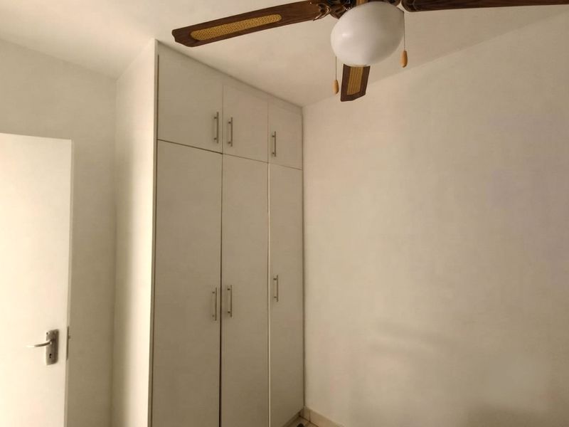A clean, empty bedroom featuring a white built-in wardrobe with overhead storage and a ceiling fan.