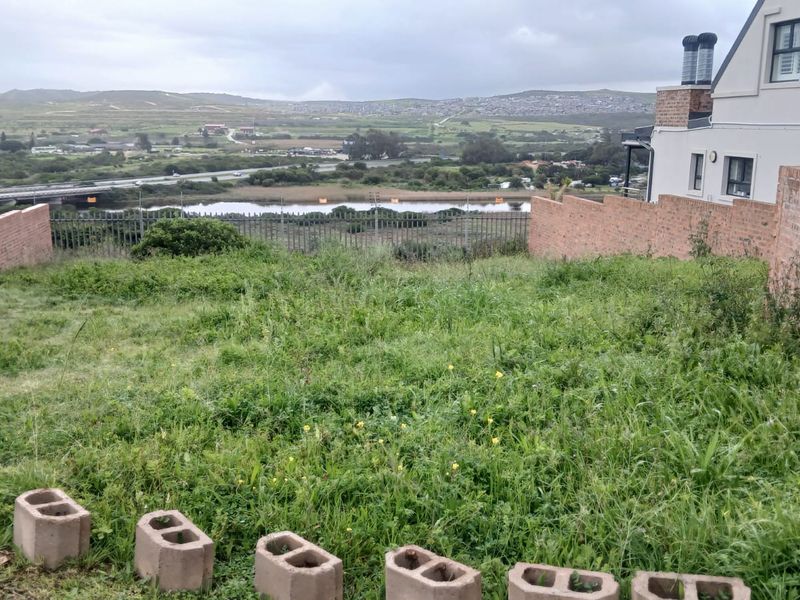 A vacant residential plot featuring brick boundary walls, metal fencing, and expansive views of the surrounding landscape and river.
