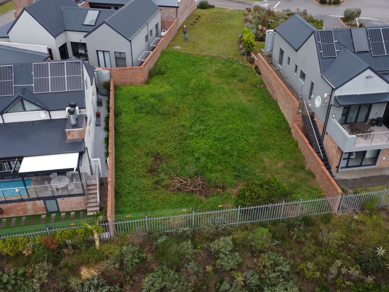 Aerial view of a vacant residential plot situated between two existing modern homes, featuring perimeter brick walls and security fencing.