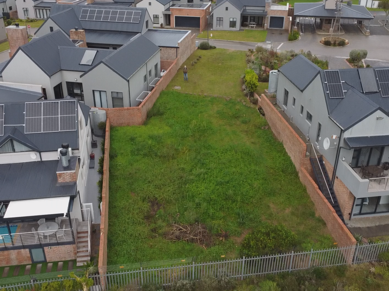 Aerial view of a vacant residential plot situated between two existing modern homes, featuring boundary walls and perimeter fencing.