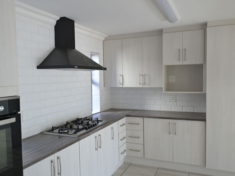 Modern kitchen featuring light wood-grain cabinetry, dark laminate countertops, subway tile backsplash, and integrated stainless steel appliances including a gas hob and oven.