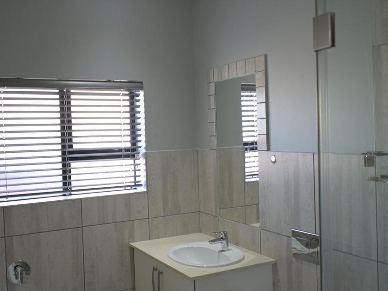Modern bathroom featuring a vanity cabinet with integrated basin, wall-mounted toilet, glass shower enclosure, bathtub, and neutral tiled finishes.