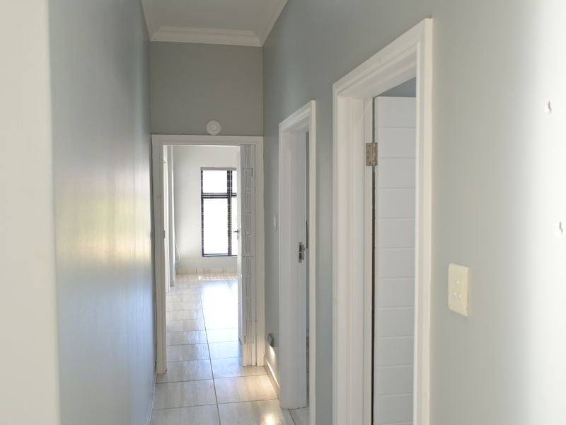 A bright, empty hallway featuring tiled flooring, neutral wall paint, and multiple internal door access points leading to other rooms.