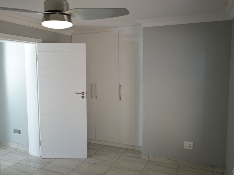A clean, neutral bedroom featuring built-in cupboards, modern tiled flooring, and a ceiling fan, offering a blank canvas for personalization.