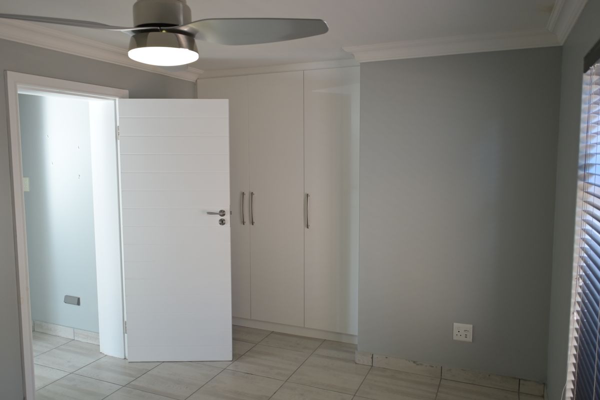 A clean, neutral bedroom featuring built-in cupboards, modern tiled flooring, and a ceiling fan, offering a blank canvas for personalization.