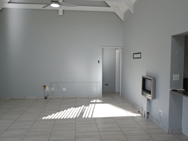 An empty living room featuring a vaulted ceiling, ceiling fan, and neutral tiled flooring, offering a blank canvas for interior design.