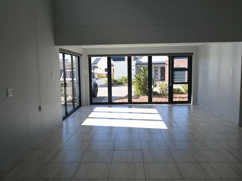 Spacious, empty living area featuring neutral tiled flooring and large aluminium stacker doors that provide abundant natural light and access to the exterior.