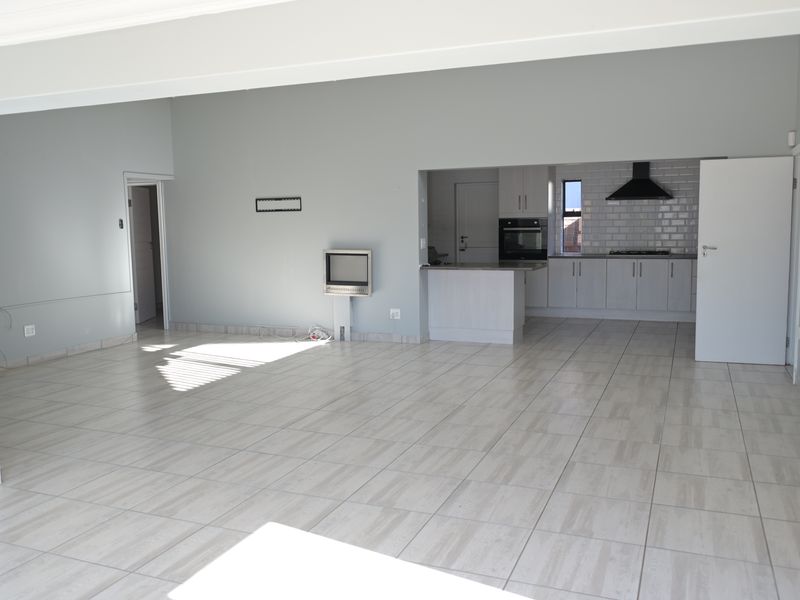 Spacious open-plan living area featuring light-toned tiled flooring and a modern kitchen with built-in appliances, subway tile backsplash, and a functional kitchen island.