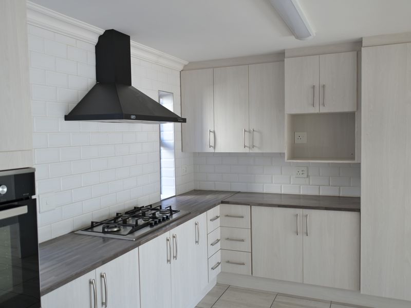 Modern kitchen featuring light wood-grain cabinetry, dark laminate countertops, subway tile backsplash, gas hob, extractor fan, and built-in oven.