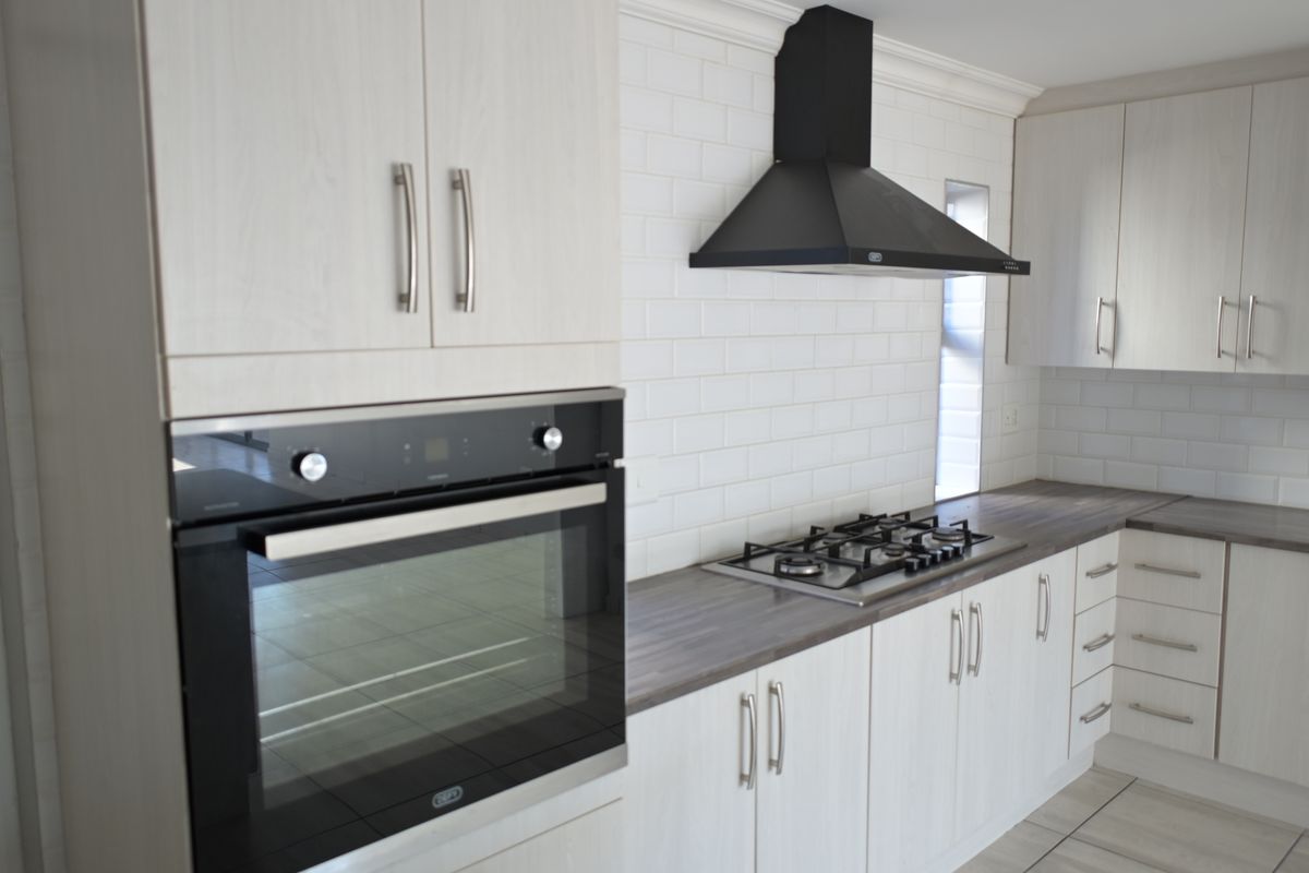 Modern kitchen featuring light wood-grain cabinetry, dark laminate countertops, subway tile backsplash, built-in oven, and gas hob with a sleek black extractor fan.