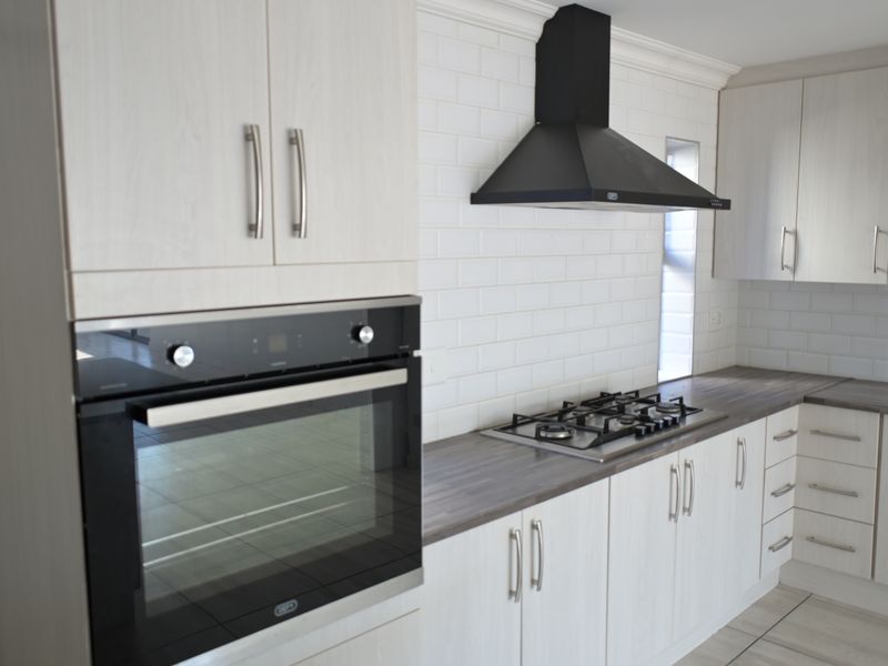 Modern kitchen featuring light wood-grain cabinetry, dark laminate countertops, subway tile backsplash, built-in oven, and gas hob with a sleek black extractor fan.