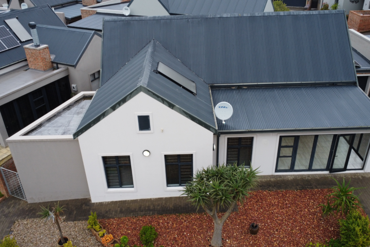 Aerial view of a modern residential property featuring a corrugated metal roof, solar panels, paved driveway, and well-maintained exterior finishes.