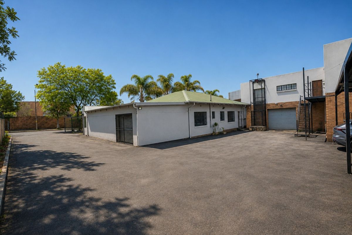 Rear exterior view of the industrial property featuring a large asphalt yard, secure access gates, roller shutter door, and external metal staircase access.