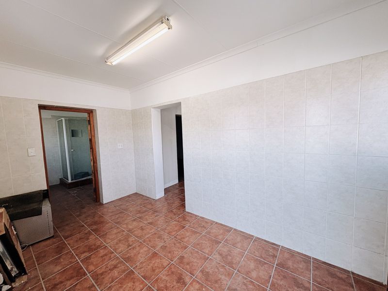 A functional utility or laundry area featuring tiled walls and flooring, with an adjacent shower cubicle and overhead fluorescent lighting.
