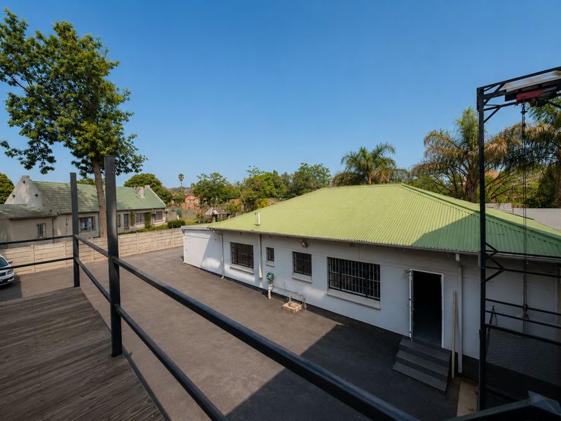 Exterior view of an industrial property featuring a corrugated metal roof, security bars on windows, and a paved driveway area with a raised deck.