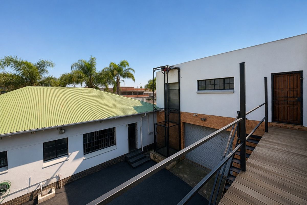Rear exterior view of an industrial property featuring a goods lift, roller shutter door, and elevated timber deck access.
