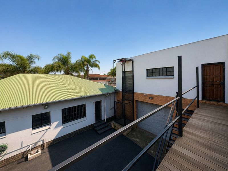 Rear exterior view of an industrial property featuring a goods lift, roller shutter door, and elevated timber deck access.
