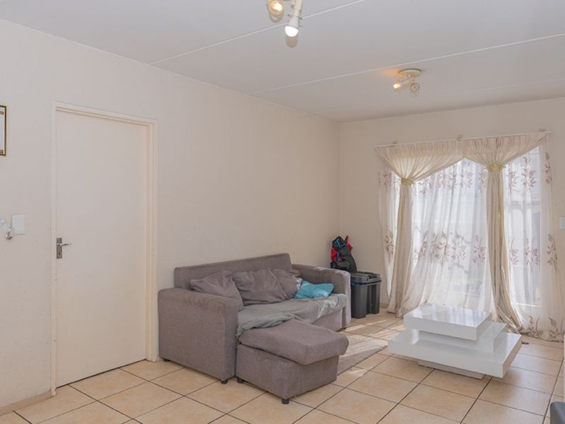A living room featuring tiled flooring, neutral walls, and a sliding door providing natural light.