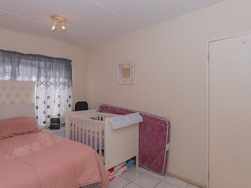 A functional bedroom featuring tiled flooring, a standard door, and a ceiling-mounted light fixture.