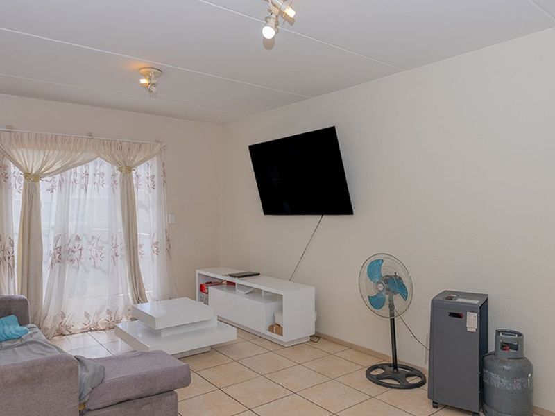 A living room featuring tiled flooring, a sliding glass door with curtains, and wall-mounted lighting fixtures.