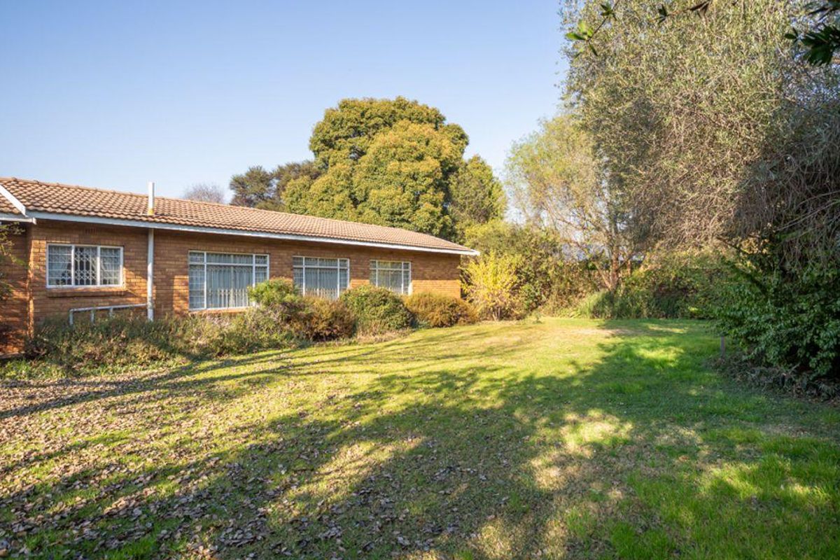 A view of the rear exterior of the house, featuring a brick facade, tiled roof, and a spacious, established garden area.