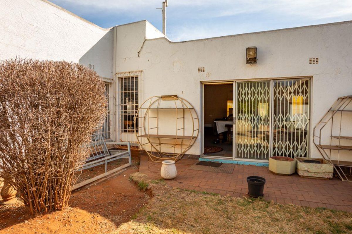 Rear exterior view of the property featuring a paved patio area, sliding glass doors with security gates, and a small garden space.