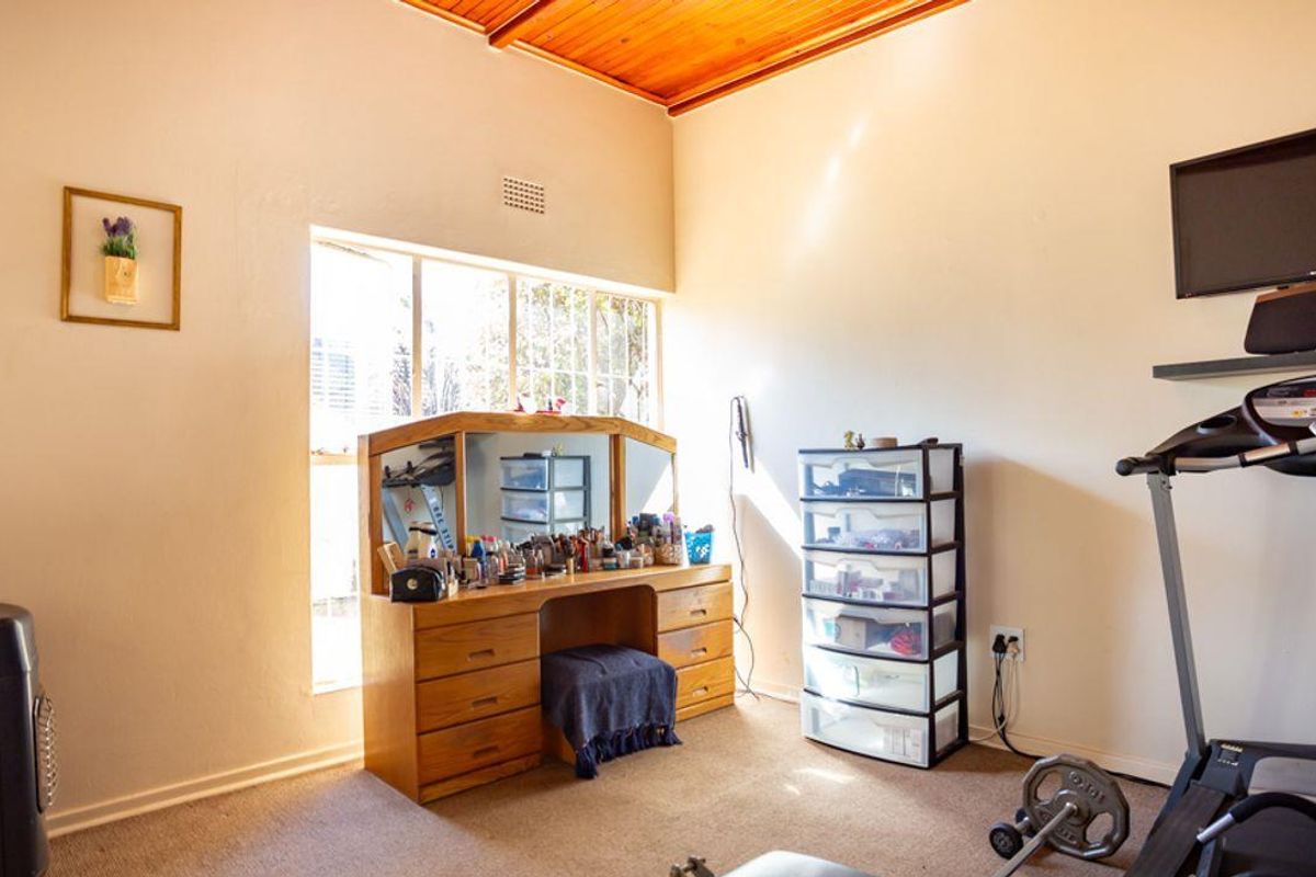 A bedroom featuring a high timber-clad ceiling, large window, and carpeted flooring, currently utilized as a multi-purpose space.