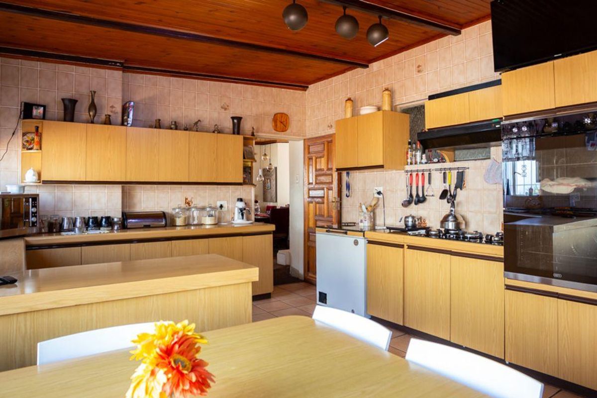 A functional kitchen featuring light wood cabinetry, built-in oven, gas hob, and a tiled backsplash, with a warm timber-paneled ceiling.