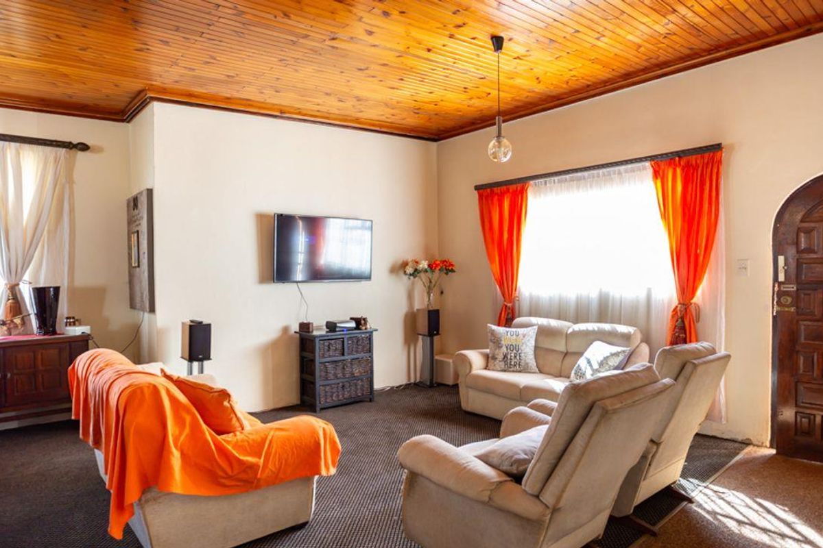A living room featuring a distinctive timber-paneled ceiling, carpeted flooring, and a solid wood arched entrance door.