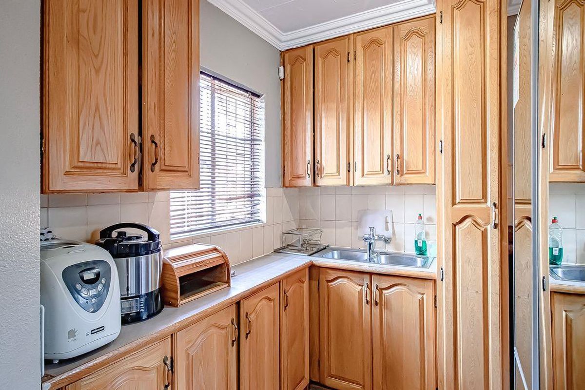 A functional kitchen featuring traditional timber cabinetry, tiled splashbacks, and a stainless steel sink, offering practical storage and workspace.
