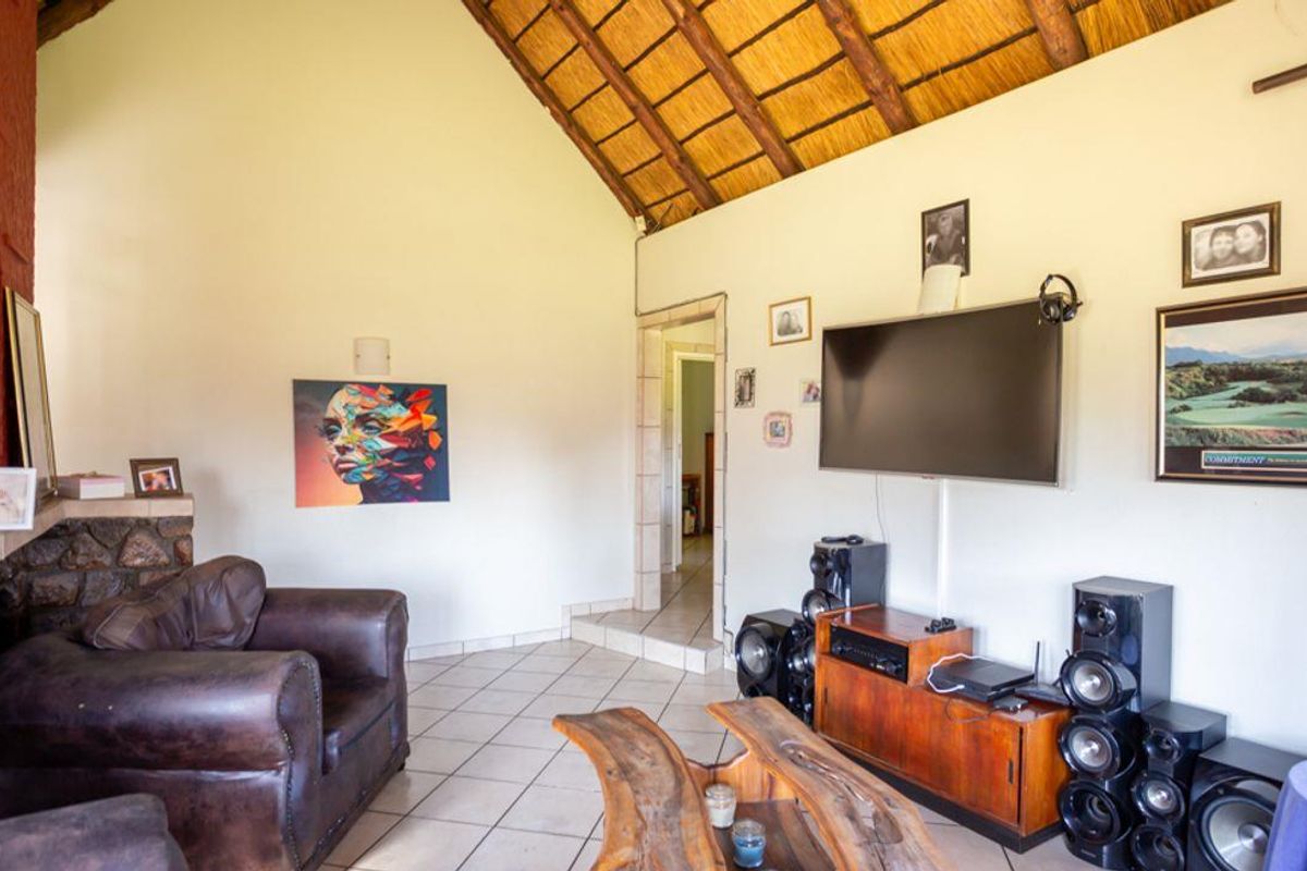 A living room featuring a high vaulted thatched ceiling, tiled flooring, and a stone-clad fireplace feature.