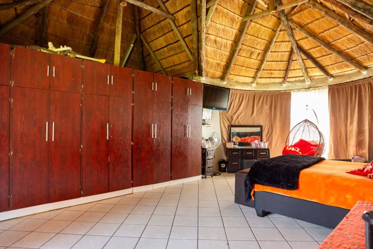 Spacious bedroom featuring a unique vaulted thatched roof, tiled flooring, and extensive built-in wooden cabinetry for ample storage.
