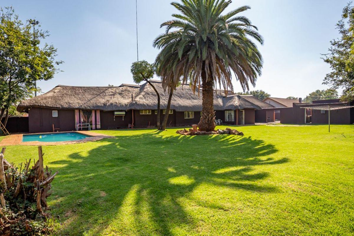 Spacious rear garden featuring a swimming pool, mature palm tree, and a large house with a traditional thatched roof.
