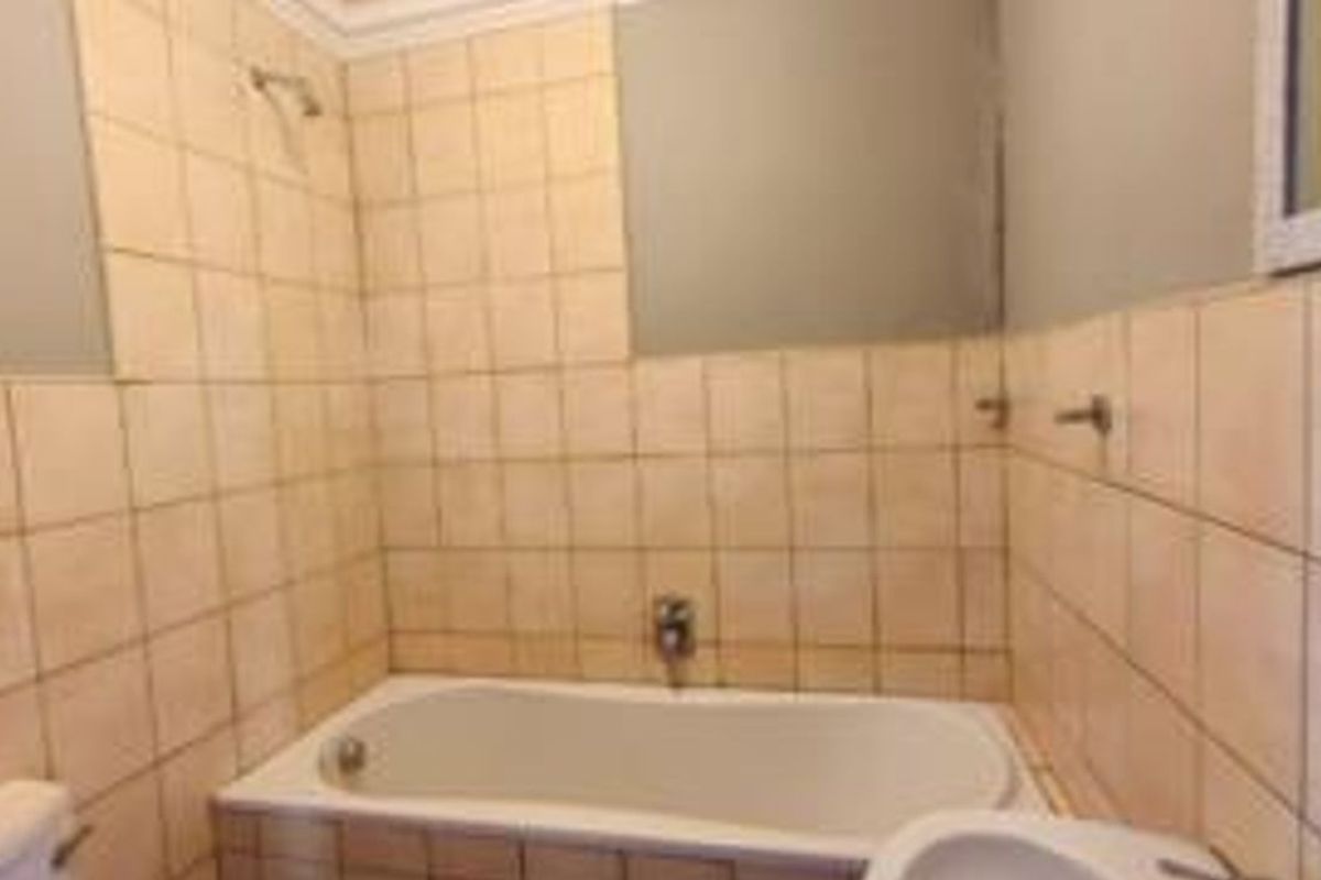 A functional bathroom featuring a built-in bathtub with shower mixer, tiled walls, and standard sanitary fixtures.