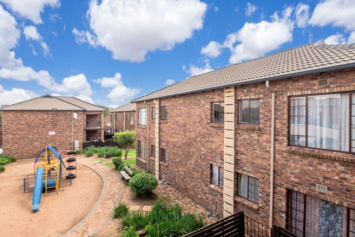 Exterior view of a brick apartment complex featuring a communal garden area with a playground and paved pathways.