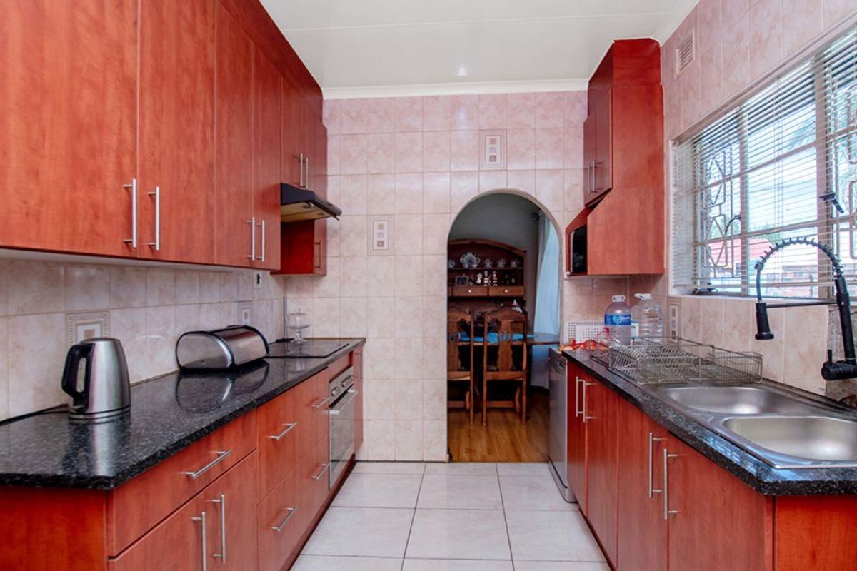 A galley-style kitchen featuring cherry wood cabinetry, dark granite countertops, a double stainless steel sink, and tiled walls and flooring.