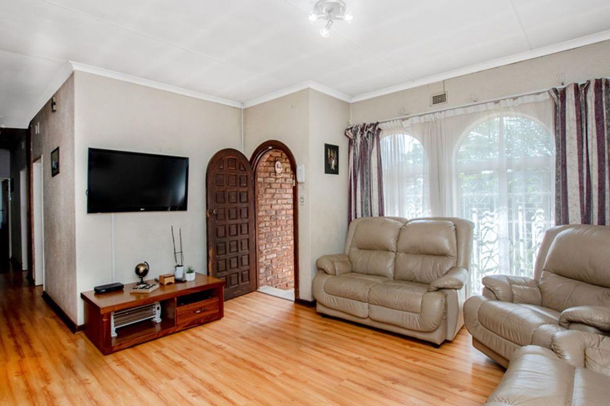 A living room featuring laminate wood flooring, arched doorway with exposed brick detail, and large arched windows allowing natural light.