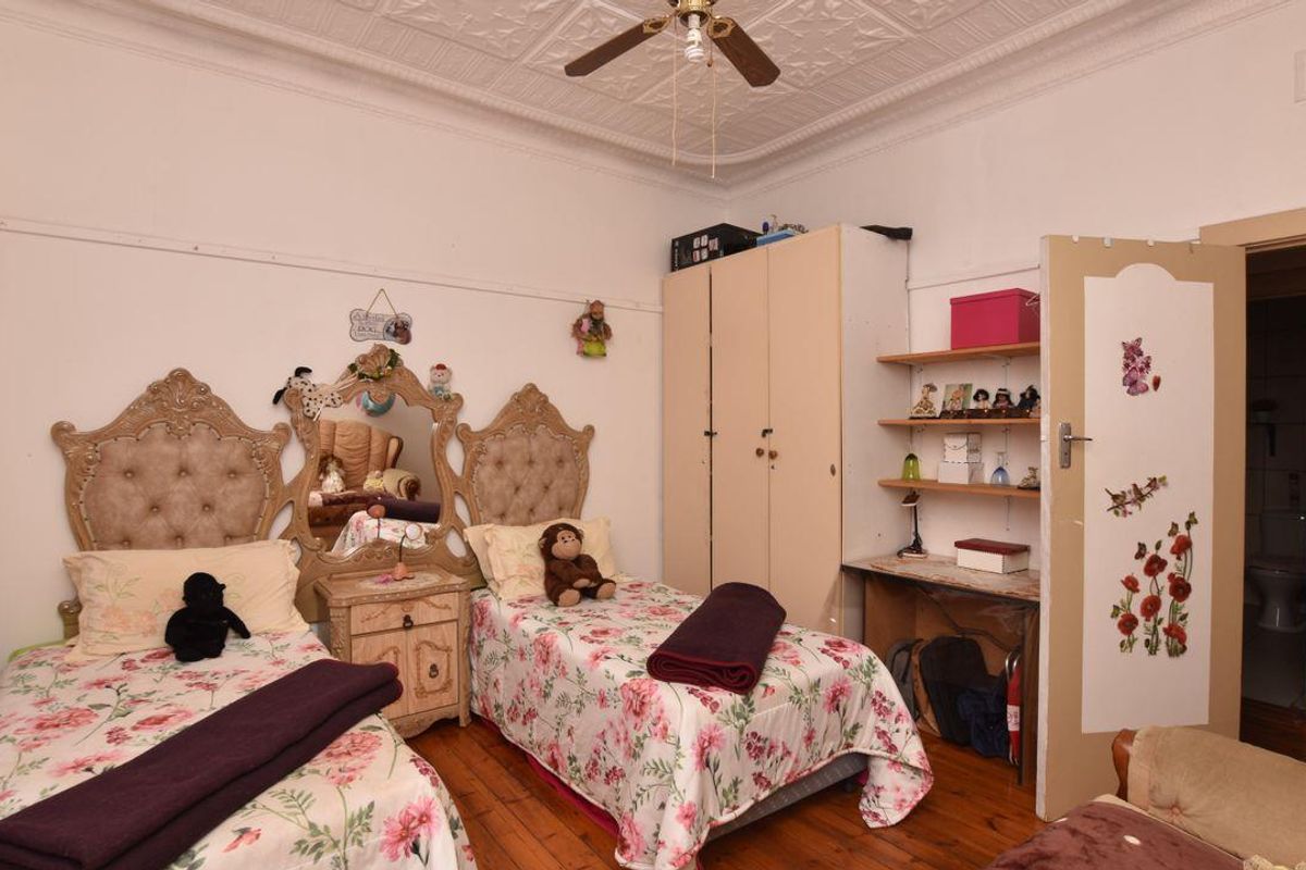 A bedroom featuring original timber flooring, decorative pressed metal ceiling, and a ceiling fan, offering a classic architectural character.