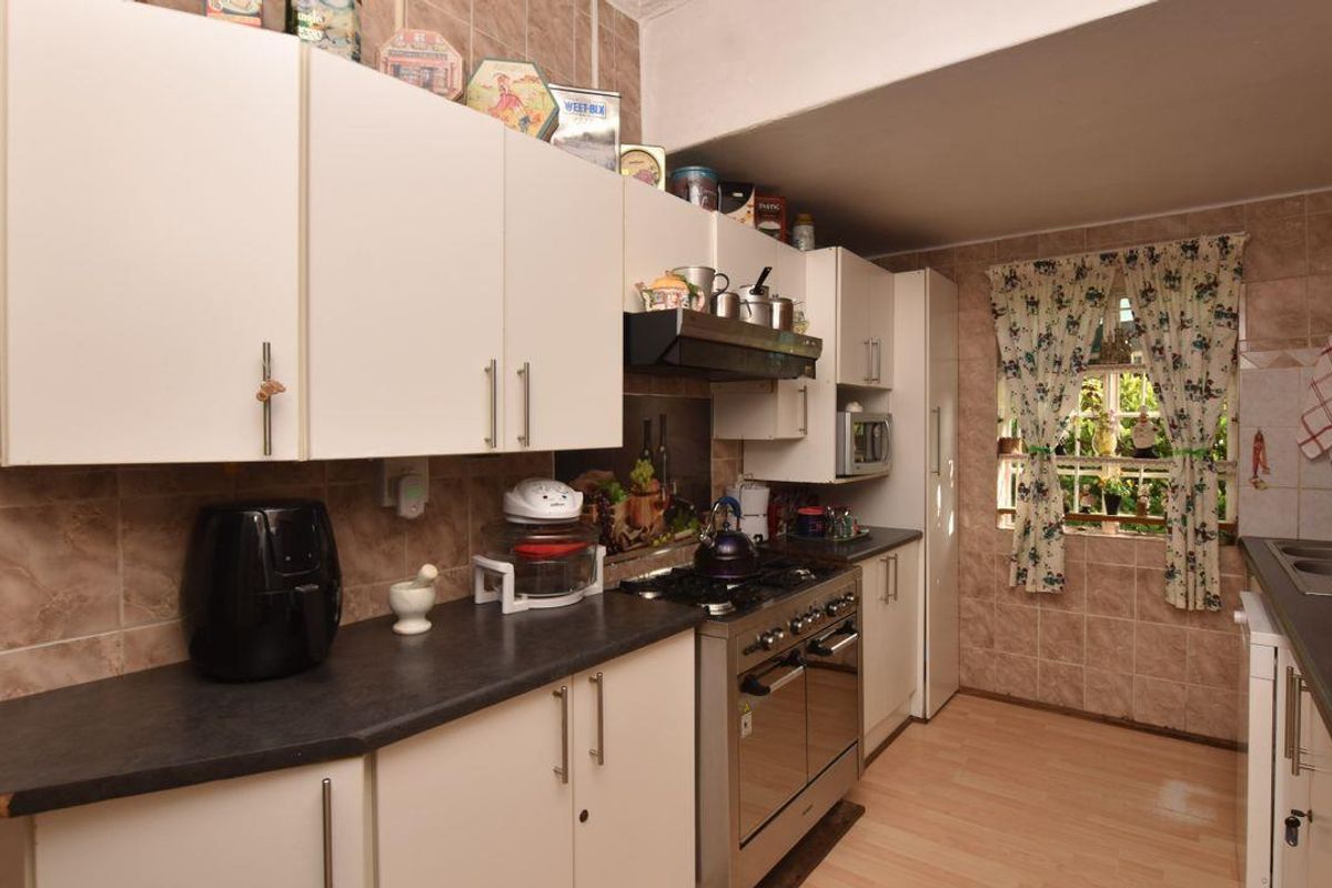 A functional kitchen featuring white cabinetry, dark laminate countertops, a built-in gas stove with extractor fan, and tiled wall finishes.