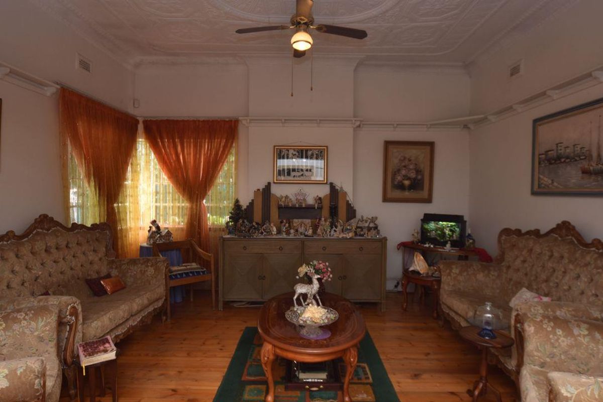 A traditional living room featuring original timber flooring, ornate ceiling detailing, and a central ceiling fan, offering a classic and character-filled living space.