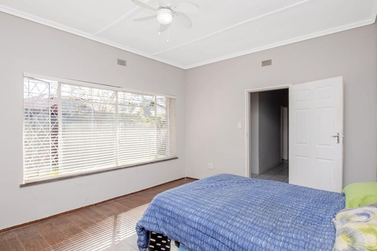 A bedroom featuring tiled flooring, a ceiling fan, and large windows with security bars, providing natural light.