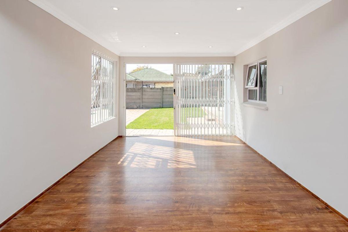 A bright, empty living area featuring wood-look laminate flooring, recessed ceiling lighting, and a sliding door providing direct access to the rear garden.