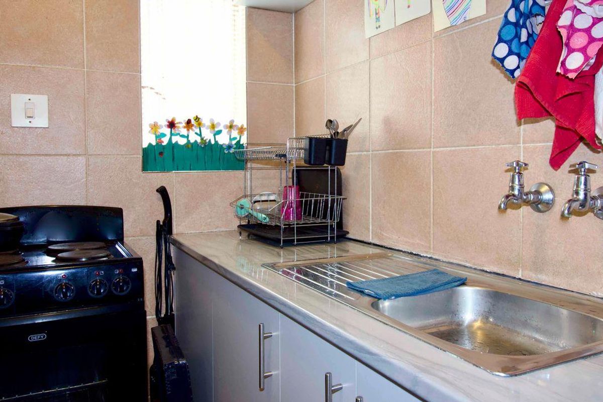 A functional kitchen area featuring tiled walls, a stainless steel sink with wall-mounted taps, and a built-in stove.